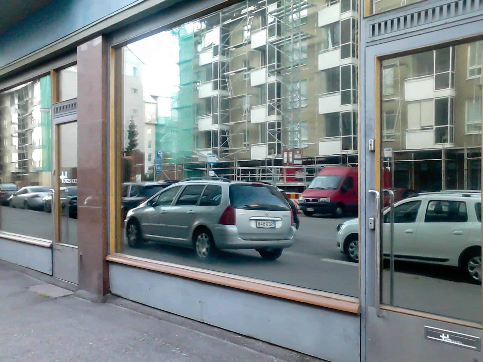 Kaupan ikkuna, jossa heijastuu katu ja parkkipaikka, taustalla rakennustyömaa.